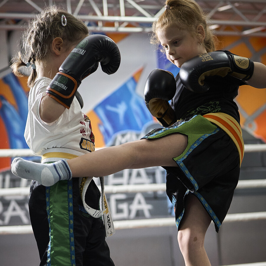 Zwei kleine Mädchen üben zu zweit einen Tritt, beide mit Boxhandschuhen