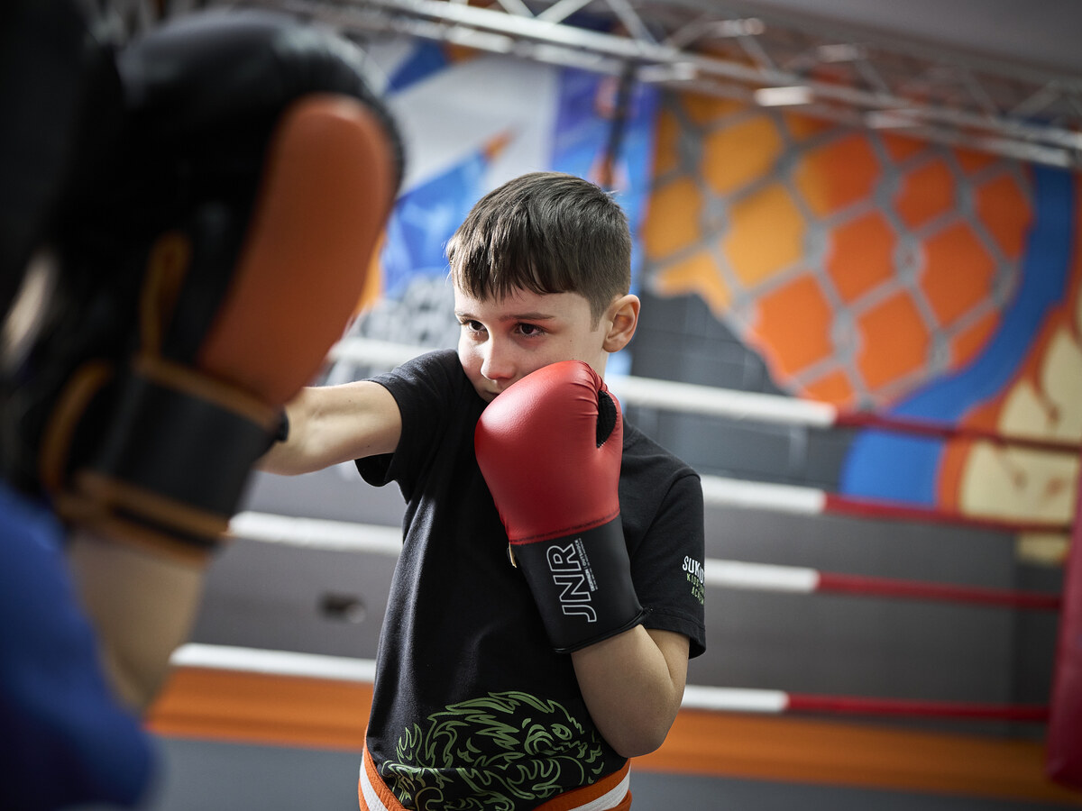 Ein Junge in Grundstellung mit roten Boxhandschuhen übt konzentriert mit seinem Partner