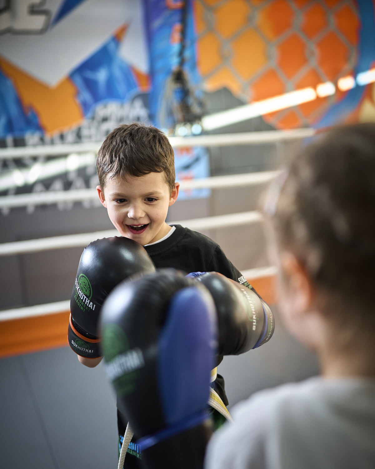 Ein Mädchen lacht beim Training in der Sukhothai Academy und streckt den Boxhandschuh nach vorn zu seiner Übungspartnerin