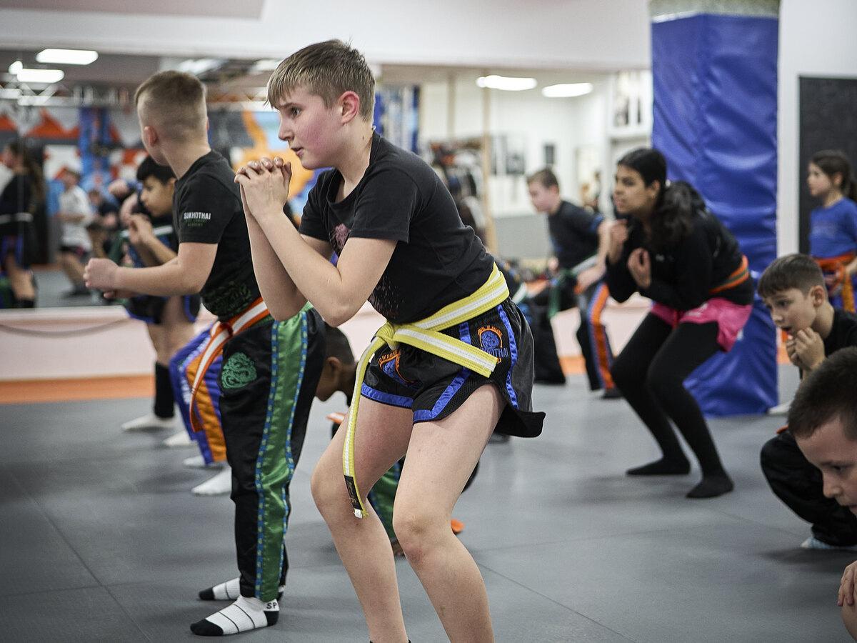 Kinder in Trainingskleidung üben gemeinsam eine Grundstellung in der Halle der Sukhothai Academy